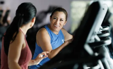 two women walking on treadmills and engaged in conversation