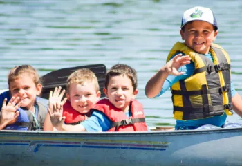 group of young kids waving from canoe on the lake