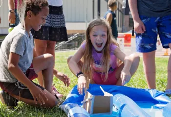 photo of boy and girl racing their cardboard boat