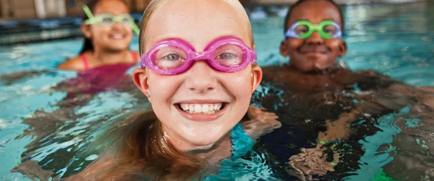 three kids wearing goggles in the pool smiling