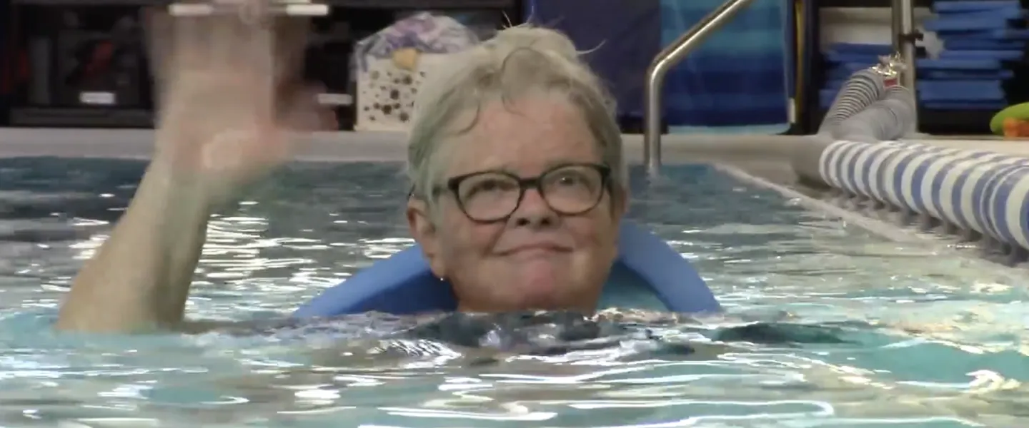 elderly woman waving from an indoor swimming pool