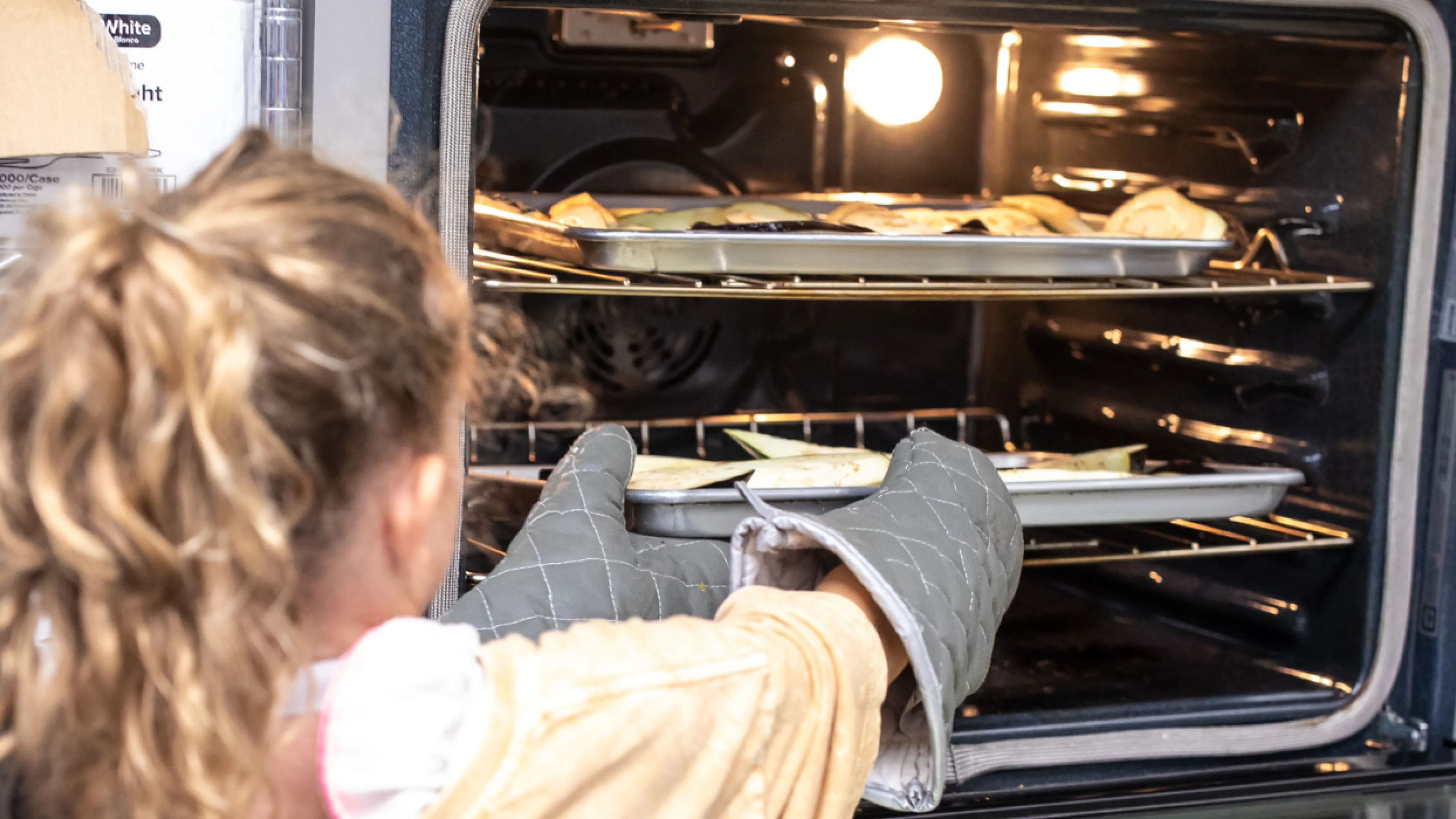 girl in kitchen removing food from oven