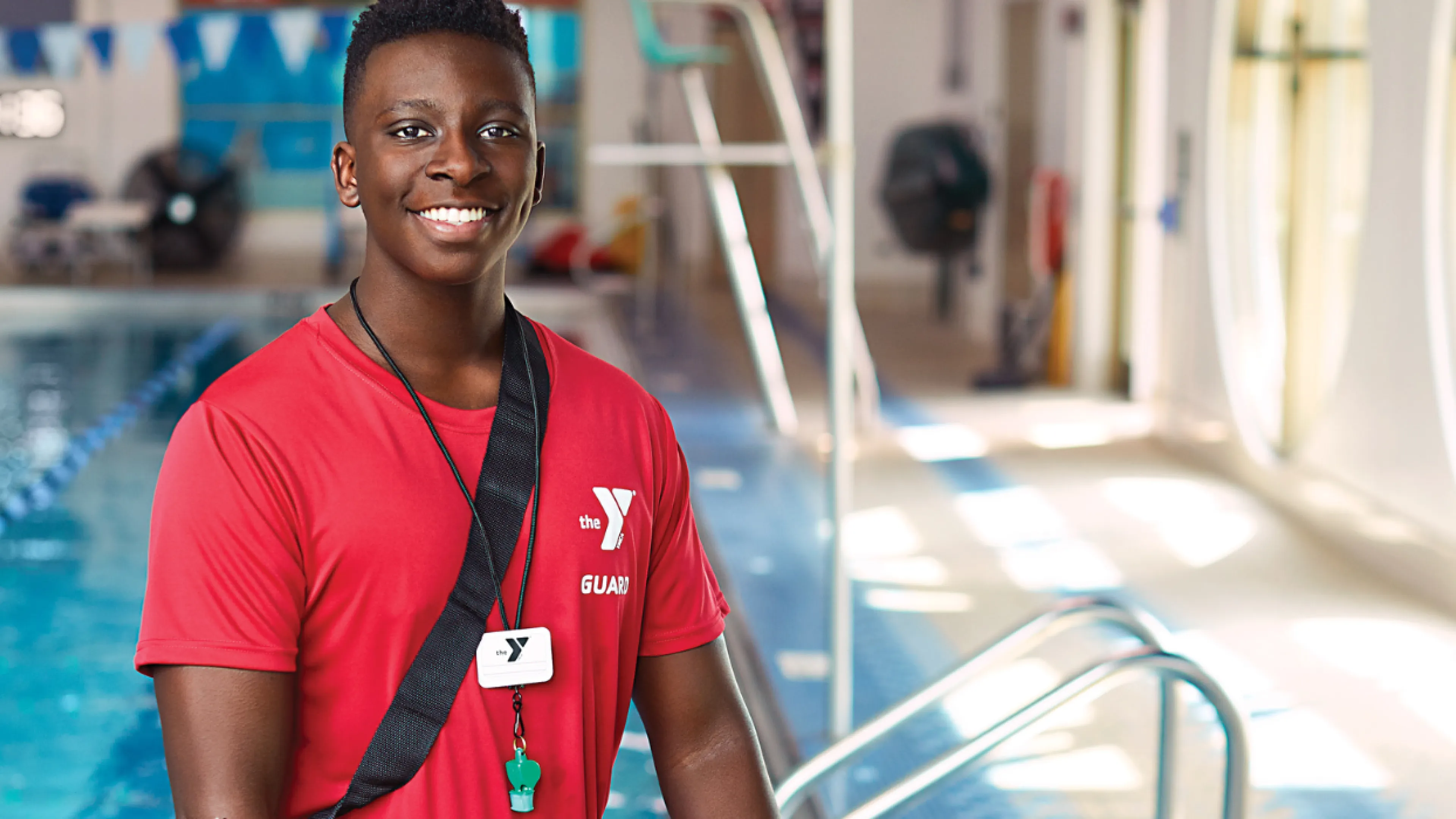 teen lifeguard standing in front of the pool smiling