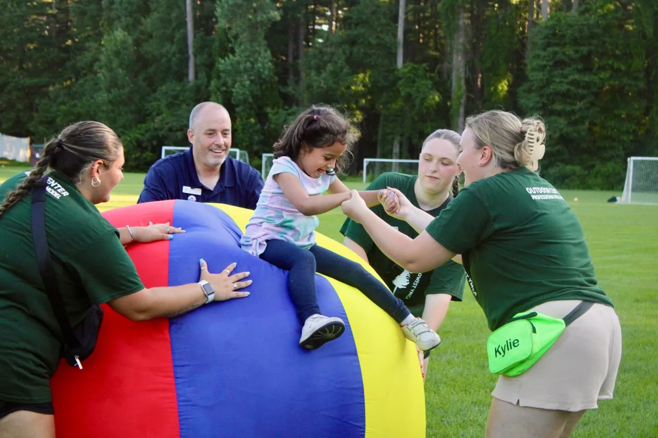 image of camp staff helping young girl slide off large bouncy ball