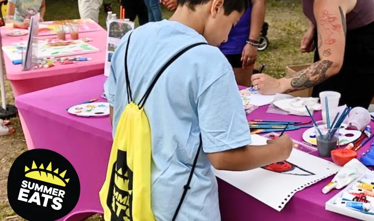 up close photo of boy painting at a table during summer eats kickoff party